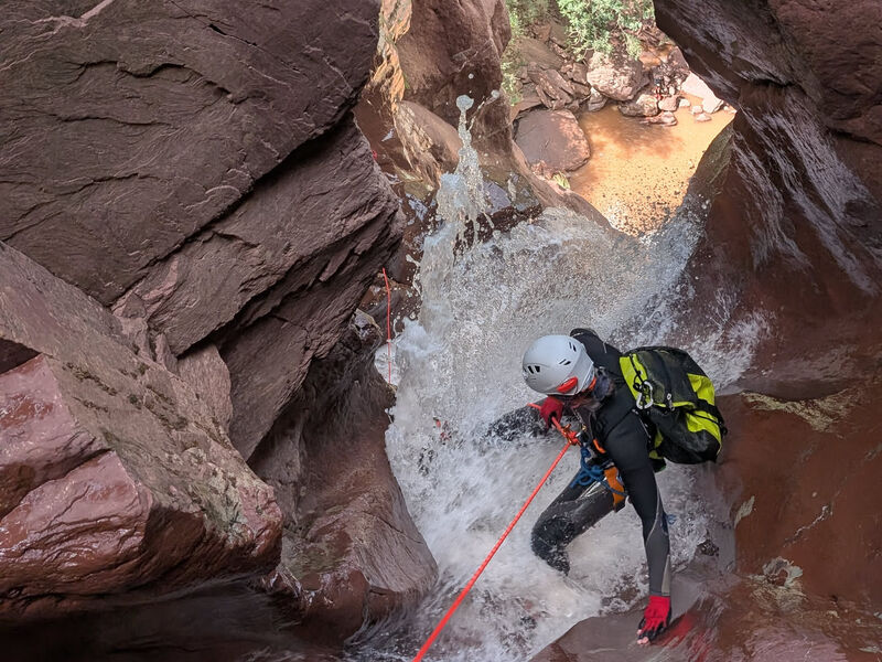 Canyoniste en rappel dans une cascade entre des parois de grès rouge